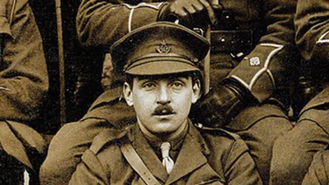 Adrian Maasz Man with short moustache and cap. Wearing military uniform and tie. 