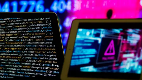 Composite image meant to represent computer software and hardware. On the left is a screen showing code in different colours. There is a pink hazard sign on the right of the picture.