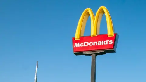 A tall yellow and red McDonald's sign with the "golden arches" symbol. The sky is blue.
