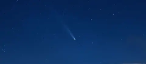 A comet appears as a glowing, streaking dot against the vast, dark, night sky