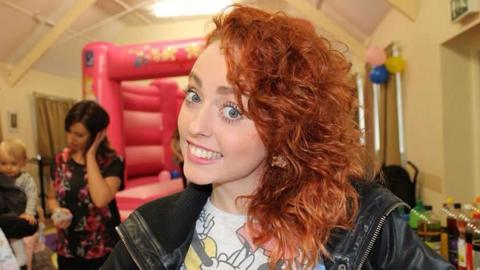 Hollie Gazzard wearing white t-shirt and standing in front of a bouncy castle with child and adults in the background.