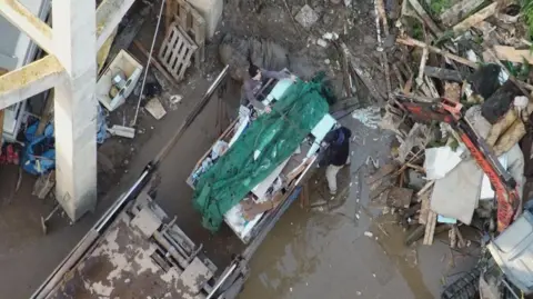 Environment Agency An aerial view of a large skip being covered by a green covering by two people. They are surrounded by waste and disused materials. 