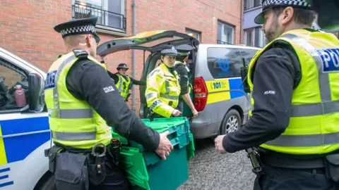 PA Media Police officers carrying green crates outside of Gordon Lamb House in Edinburgh.