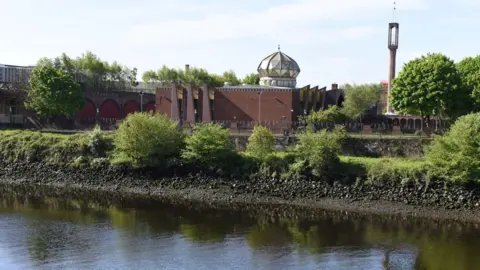 Getty Images Glasgow Central Mosque on the River Clyde. A red stone building with glass dome, surrounded by trees and a tall, slender minaret tower