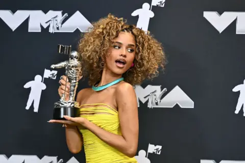 ANGELA WEISS / AFP South African singer-songwriter Tyla poses in the pressroom with the Best Afrobeats award for "Water," during the MTV Video Music Awards at UBS Arena in Elmont, New York.