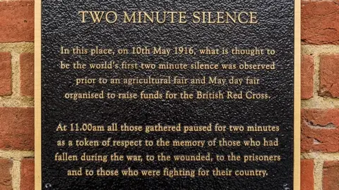 Simon Furber/BBC A black plaque with gold writing on a wall marking the world's first two-minute silence in Farnham 