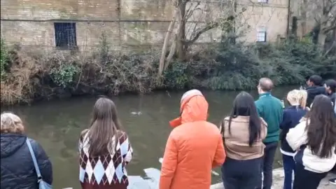 Sharron Bright/Canal & River Trust Nine people standing on a canal tow path looking at an otter in the water