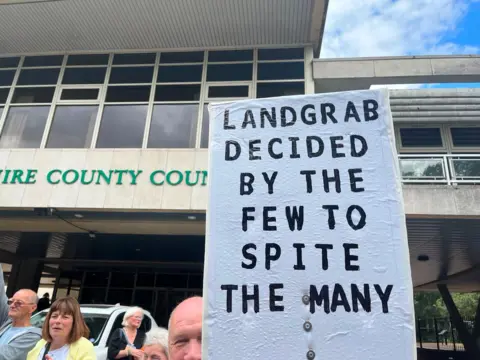 A protest sign saying "landgrab decided by the many to spit the few."