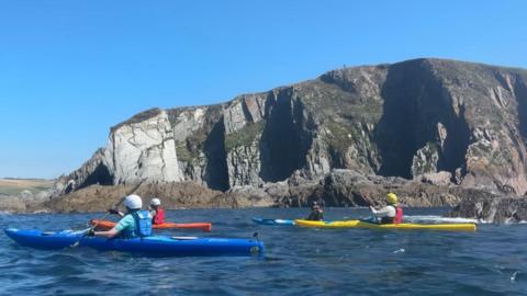 Four kayakers in the sea in front of cliffs