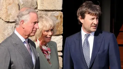 Getty Images Timothy Knatchbull stands outside a building next to King Charles and Queen Camilla. He has dark brown hair and is dressed in a dark blue suit, patterned tie and white shirt.