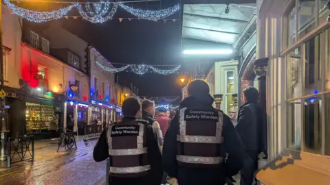 Police and Crime Commissioner Men walking through Swindon with high vis which says 'community safety warden'