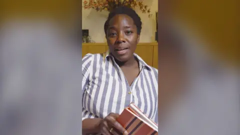 Kimberley Wilson wearing a white and blue striped shirt holding a notepad.