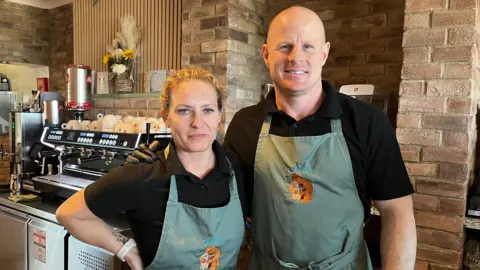 Sarah and Garry Jeffery stand in the Low Tide Coffee House in Seaham. They are dressed in matching navy aprons with black t-shirts.