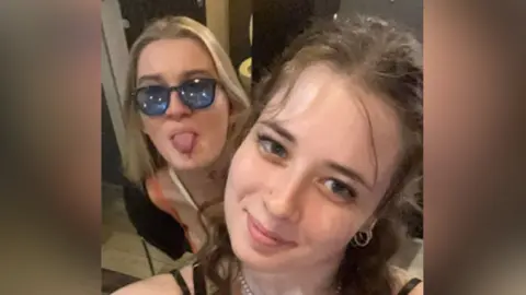 Annie Conway A selfie-style image of Annie Conway wearing tinted glasses and sticking her tongue out. In front of her is her cousin. They are both looking into the camera. 