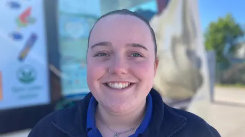 A head and shoulders photograph of Megan Kirk who is wearing a blue tshirt and a navy fleece top.