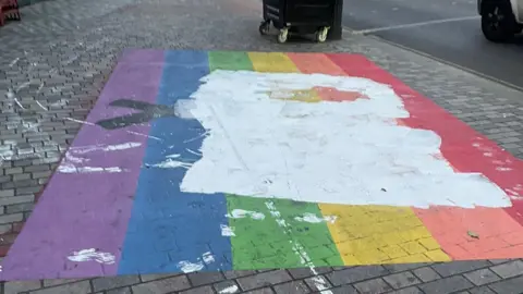 Chris Austin  A rainbow flag painted on the pavement, covered in white paint