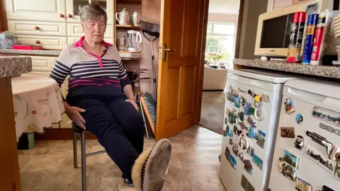 Martin Giles A woman sitting on a chair in her kitchen lifting her leg up. She is bending her recently operated-on hip