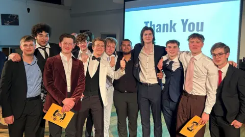 Martin Penrose A group of 11 young men look at the camera. They are all smartly dressed. Two are holding yellow cards which have a panther symbol on.