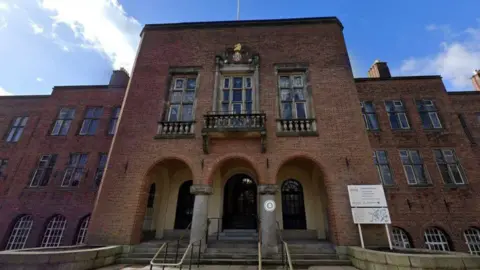 Google A large red brick building with three archways at the front and three windows above.