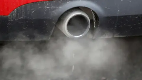 Reuters/Peter Nicholls A close up shot of a single stainless steel coloured car exhaust pipe. A plume of white fumes pours out of the exhaust with two drops of water also falling to the tarmac below.