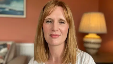 A woman with red hair looking at the camera, she has a white shirt