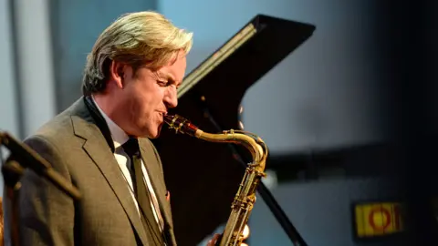 Tommy Smith, dressed in a grey suit, playing the saxophone