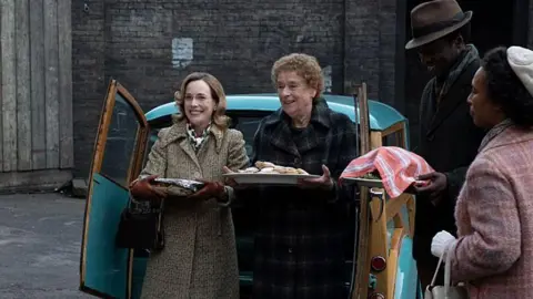 BBC/Neal Street Productions/Olly Courtney woman and woman hold two plates outside an old van