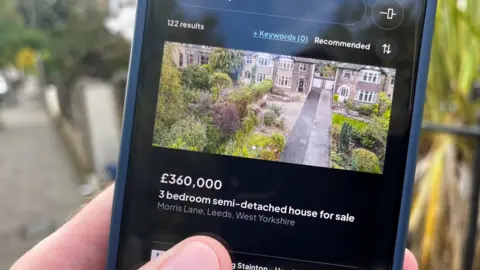 Someone holding a telephone  showing a spot   portal tract  advertizing  a £360,000 3  chamber  semi-detached location   for sale