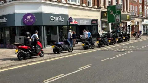 Seven mopeds parked on a kerb in a high street
