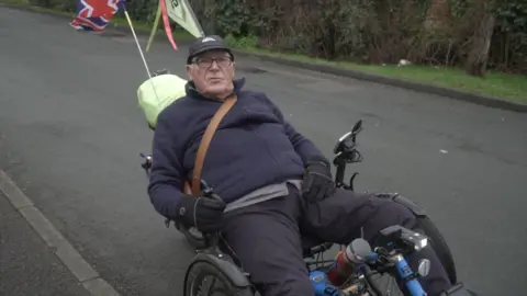 Local Democracy Reporting Service/Oliver Leader de Saxe An elderly man, wearing glasses and a dark jumper and trousers, riding an adapted bicycle. 