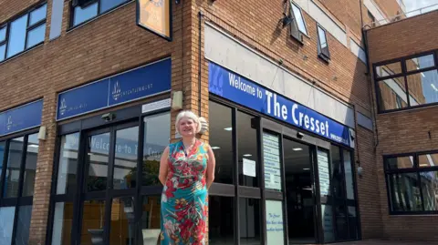 HARRIET HEYWOOD/BBC Louise Chantal is standing outside the Cresset building. It has brown bricks and electric glass doors at the entrance. She is smiling with her hands behind her back. 