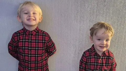 Abbie McNeill Grayson, on the left, and Dalton both have short, blond hair. They are both smiling at the camera and are both wearing red and black tartan shirts. 