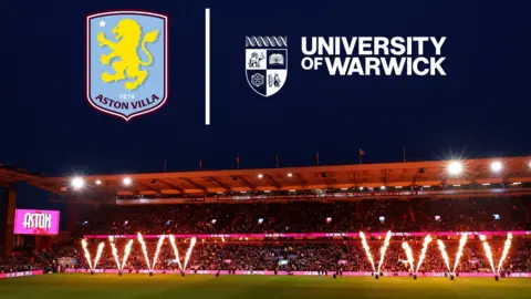 Aston Villa's Villa Park ground is lit at night with the club's logo in the upper left of the picture and the University of Warwick logo in the upper right. On the pitch, fireworks are going off before a kick-off.