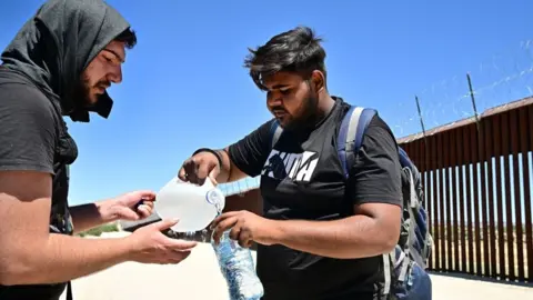 Migrants from India's Punjab region pause for water while walking beside the US-Mexico border wall at at Jacumba Hot Springs, California on June 5, 2024. Allow for syndication