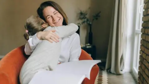 A young girl and a woman sat in an orange chair embracing, the women's eyes are closed and she is grinning