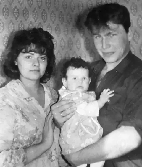 Supplied Black and white photo of Iryna and Serhiy with baby Katya. Serhiy is wearing a dark shirt and holding the baby, who has dark hair and is looking at the camera. Iryna is wearing a floral blouse.