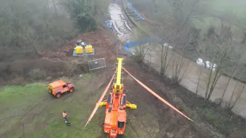 An aerial shot of an orange crane preparing to pull a narrowboat from a canal