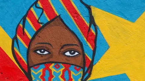 A mural showing a woman wearing a medical facemask and headwrap.
