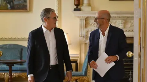 Two men (Sir Keir Starmer and Nick Robinson) look at each other as they walk through a doorway