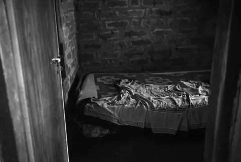 Madhuraj/Kochi Biennale Foundation A photo of a cot in a small, brick-lined room with a disheveled bedsheet lying on it.