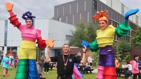 West Northamptonshire Council Two stilt walkers in colourful costumes hold hands with a man not on stilts