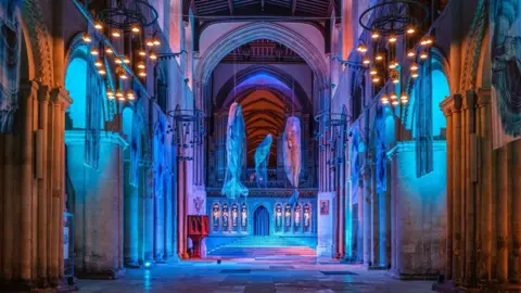 Steve Hartridge Three models of sperm whales hang in the nave of Winchester Cathedral, which has been lit in blue to recreate the ocean.