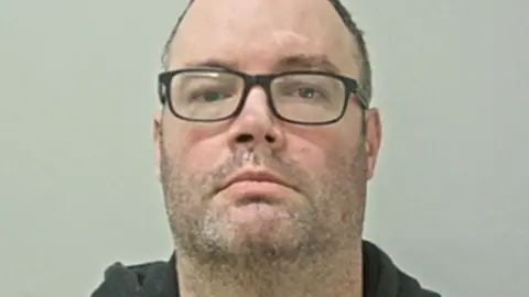 Lancashire Police Thomas Freret has dark-framed glasses, stubble and short dark hair.