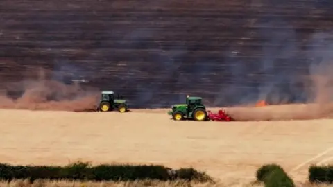 Peter Medlicott Photography Farmers in green tractors create firebreaks to stop the spread of flames in a field.