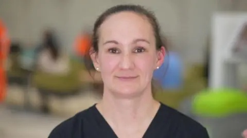 Jamie Niblock/BBC Catherine Barlow is in the middle of the image. She has brown hair in a ponytail and is wearing a black T-shirt.