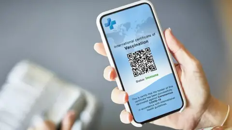 Hand holding a mobile phone showing a Covid passport QR code