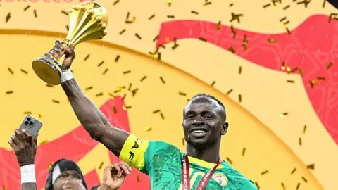 Sadio Mane smiling and holding the Africa Cup of Nations trophy up