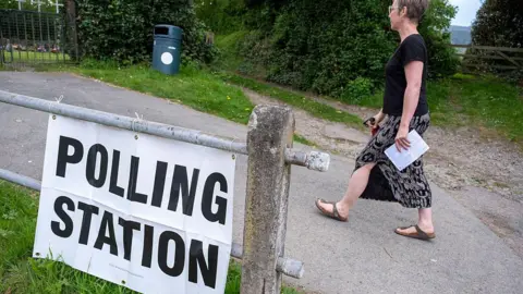 Getty Images A woman walks behind a sign on a fence reading "polling station".