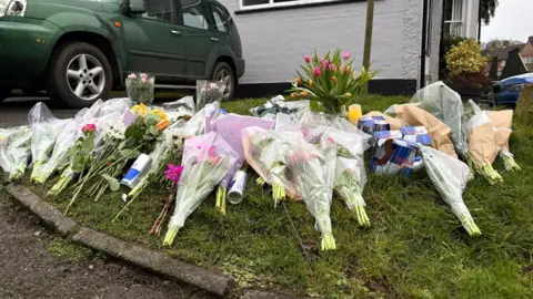 Ben Schofield/BBC A large selection of flowers on grass in Knockholt outside Three Horseshoes pub