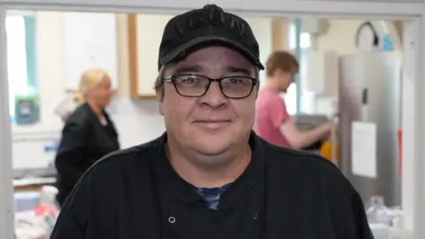 Lottie Eaton wearing black rimmed glasses, a black apron and black baseball cap.